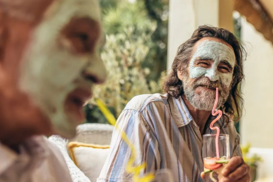 two older men wearing face masks drinking juice from straws